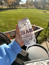 Hand holding Chaos Coordinator glass can with floral and butterfly design outdoors